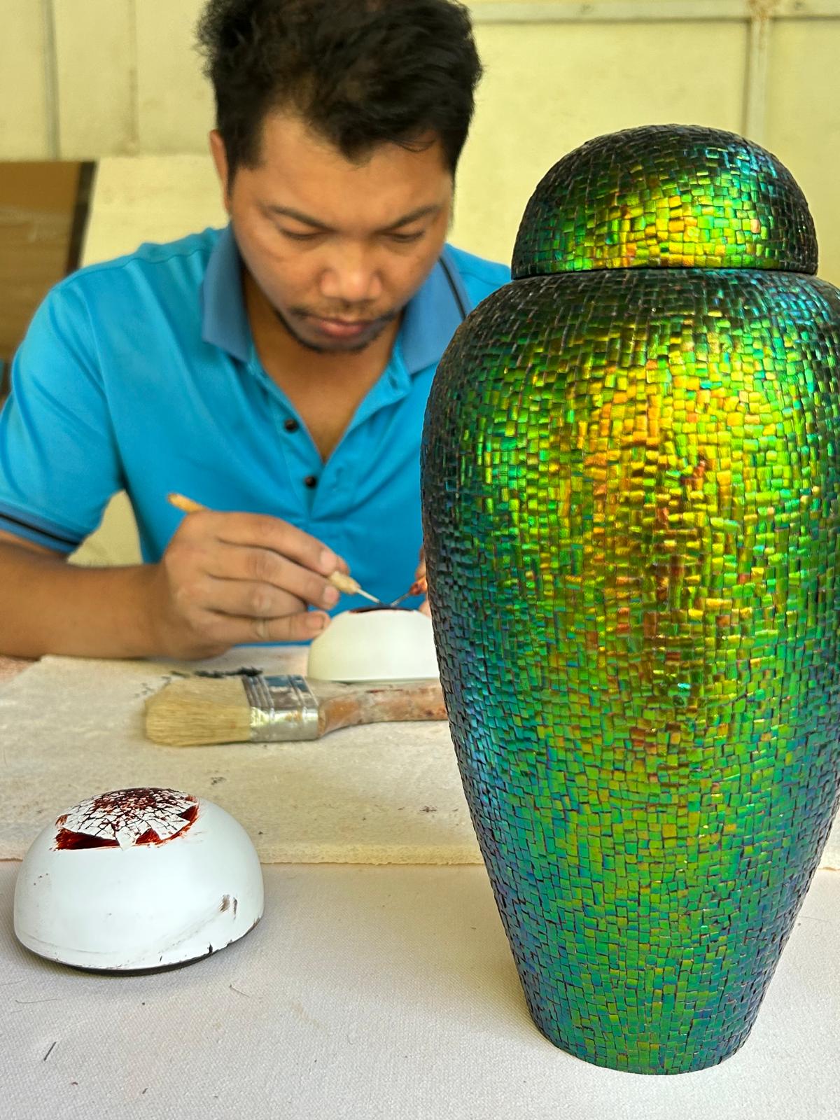 Artisan working on beetle wing inlay vase — iridescent green surface